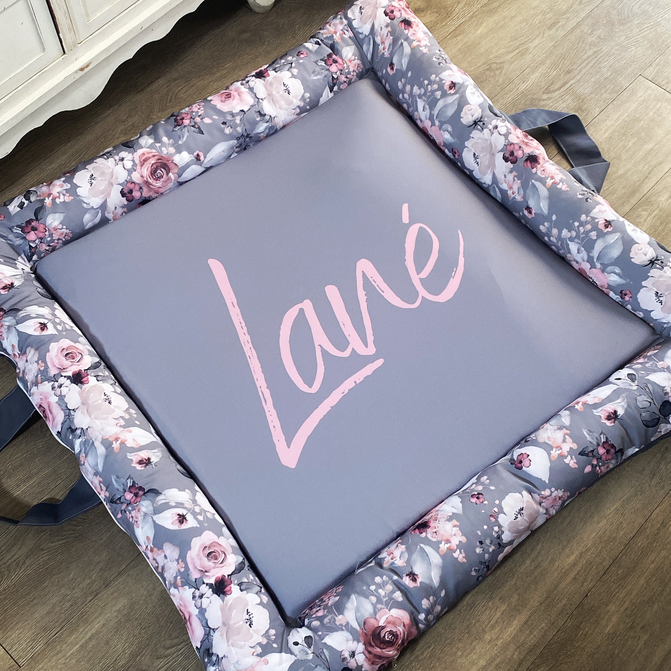 A gray baby play doughnut with a floral pattern around the edge and the name 'Lana' written in the center.