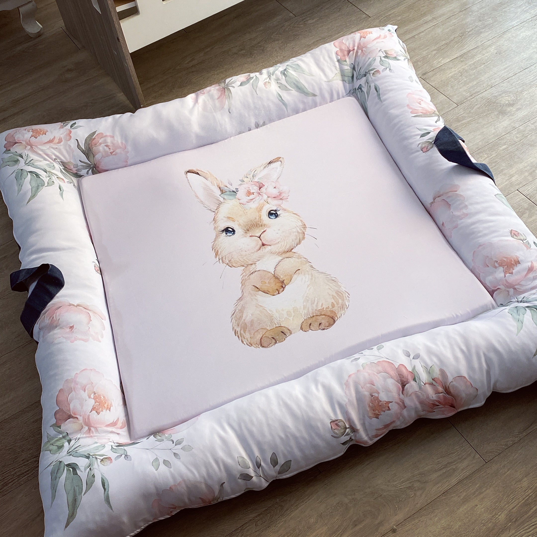 A floral-patterned baby play doughnut with a central illustration of a bunny, with washable cover and side handles.