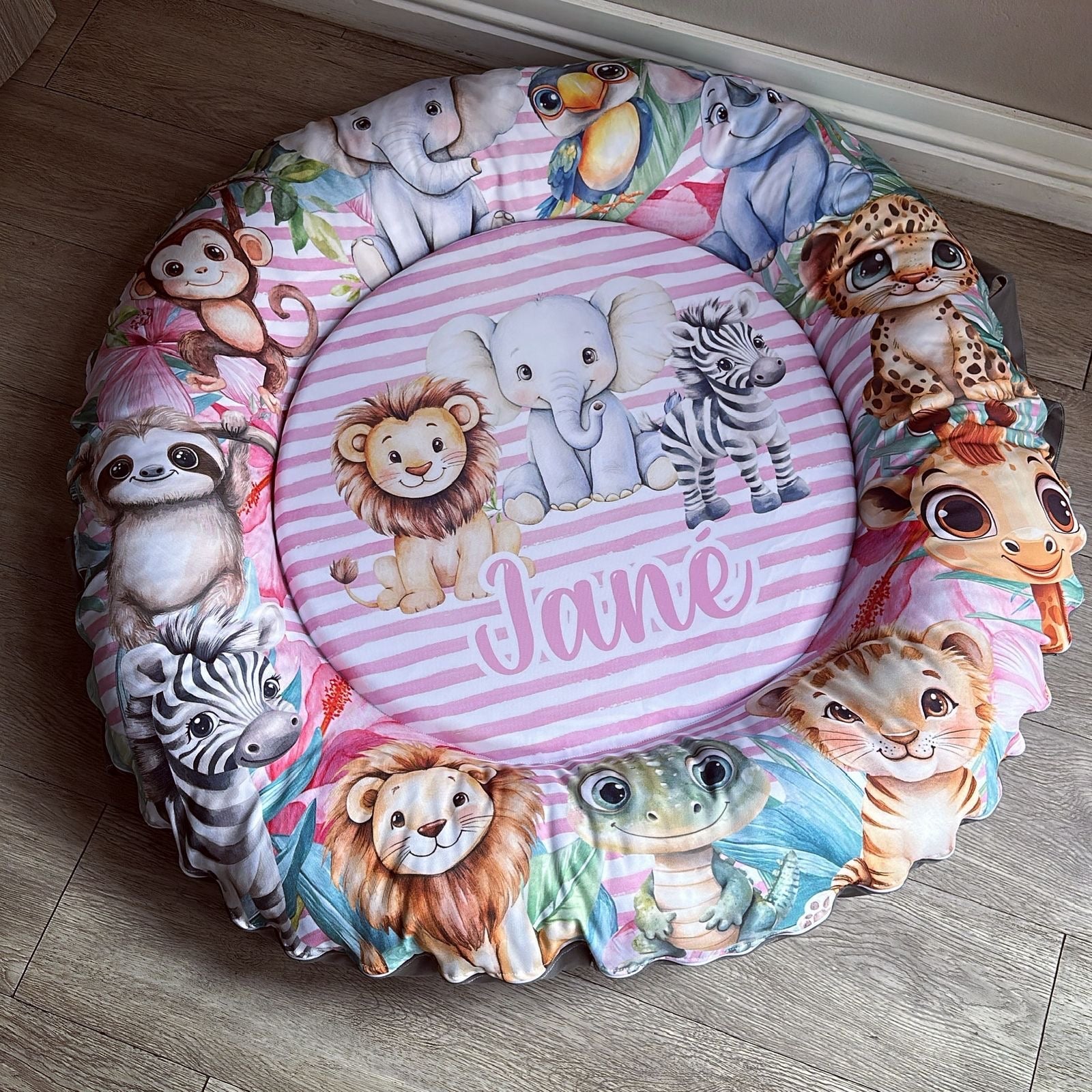 Round cushion with animal illustrations and the name 'Jane' on a wooden floor.