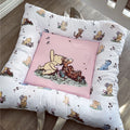 Baby crib bumper with cartoon characters and a pink pillow featuring a bear and tiger.
