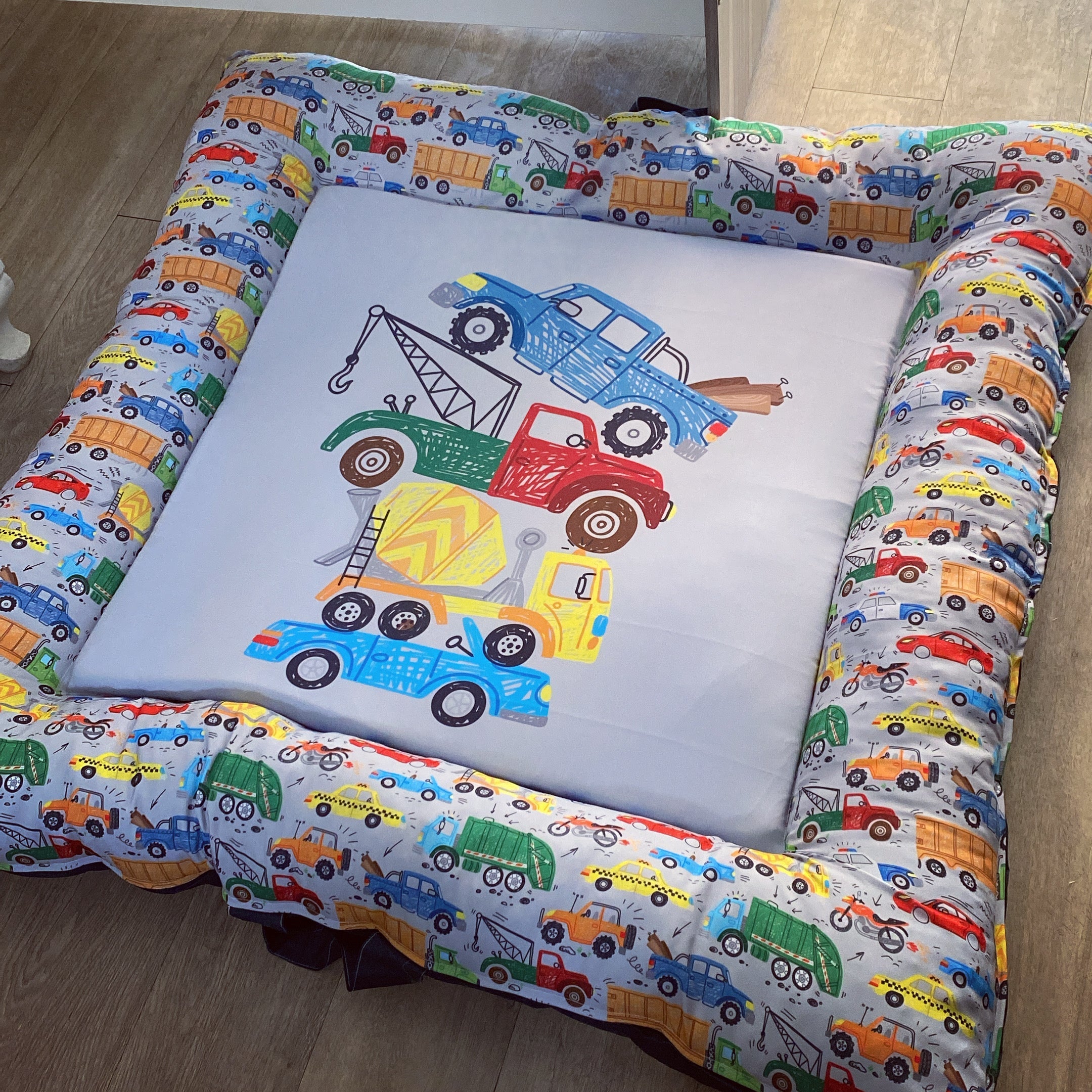 A colorful baby play doughnut with a transportation theme, featuring various vehicles such as cars, trucks, and trains in a patterned design.