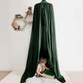 A green hanging tent canopy set up over a child lying on a mat, reading a book.