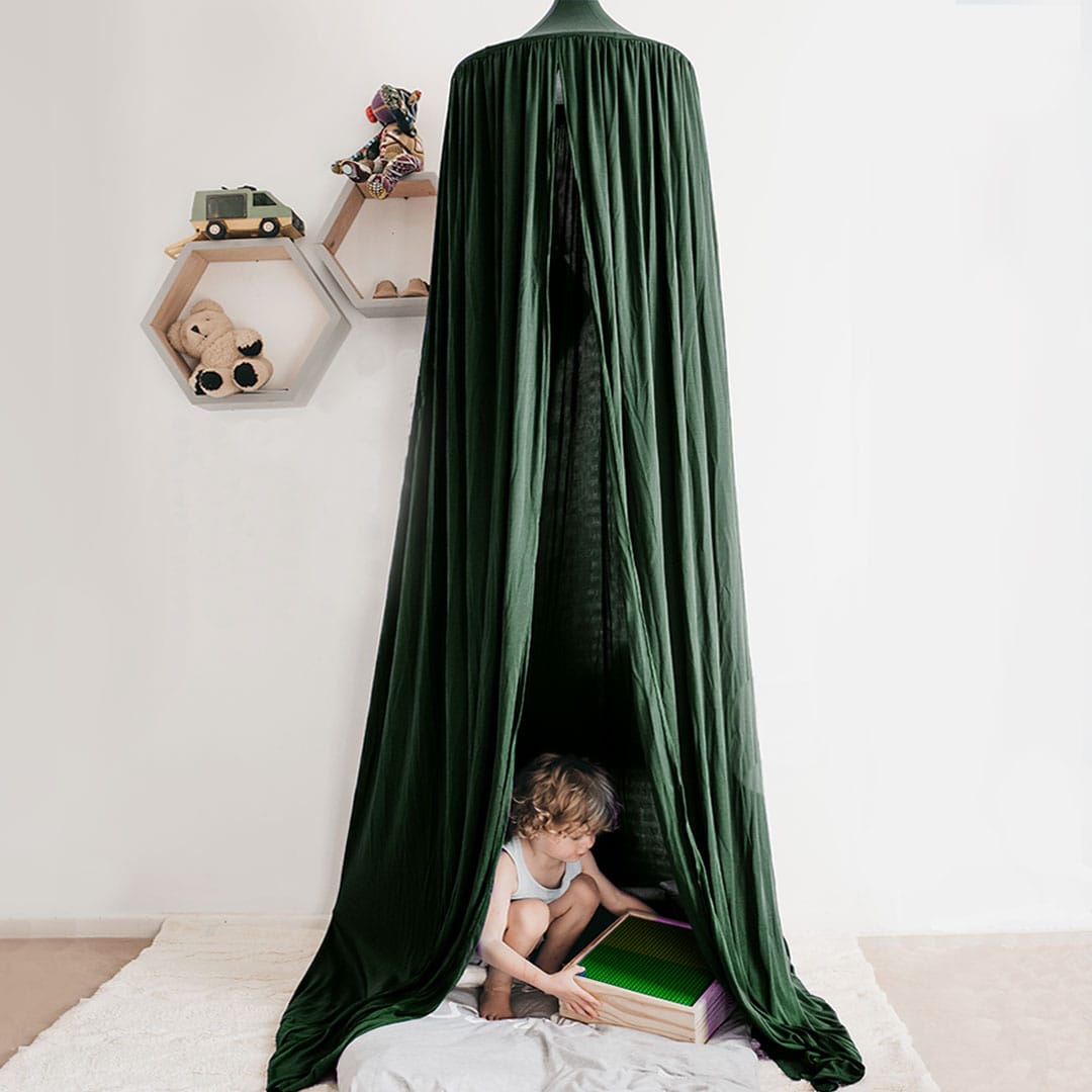 A green hanging tent canopy set up over a child lying on a mat, reading a book.