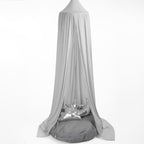 A grey hanging tent canopy with a hoop diameter of 45cm, displayed outdoors. It appears to be made of a stretchy fabric and is draped elegantly with one side featuring a metallic ornament.