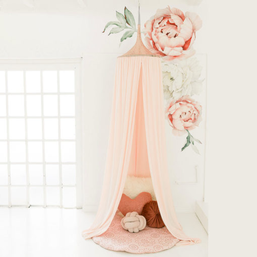 A pink hanging tent canopy with floral designs, set up in a room with a white background. It is positioned above a cream-colored feeding chair with a rose gold accent.