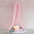 A pastel pink hanging tent canopy set up over a small table with a book and a decorative starfish, with dimly lit candles adding a warm glow.