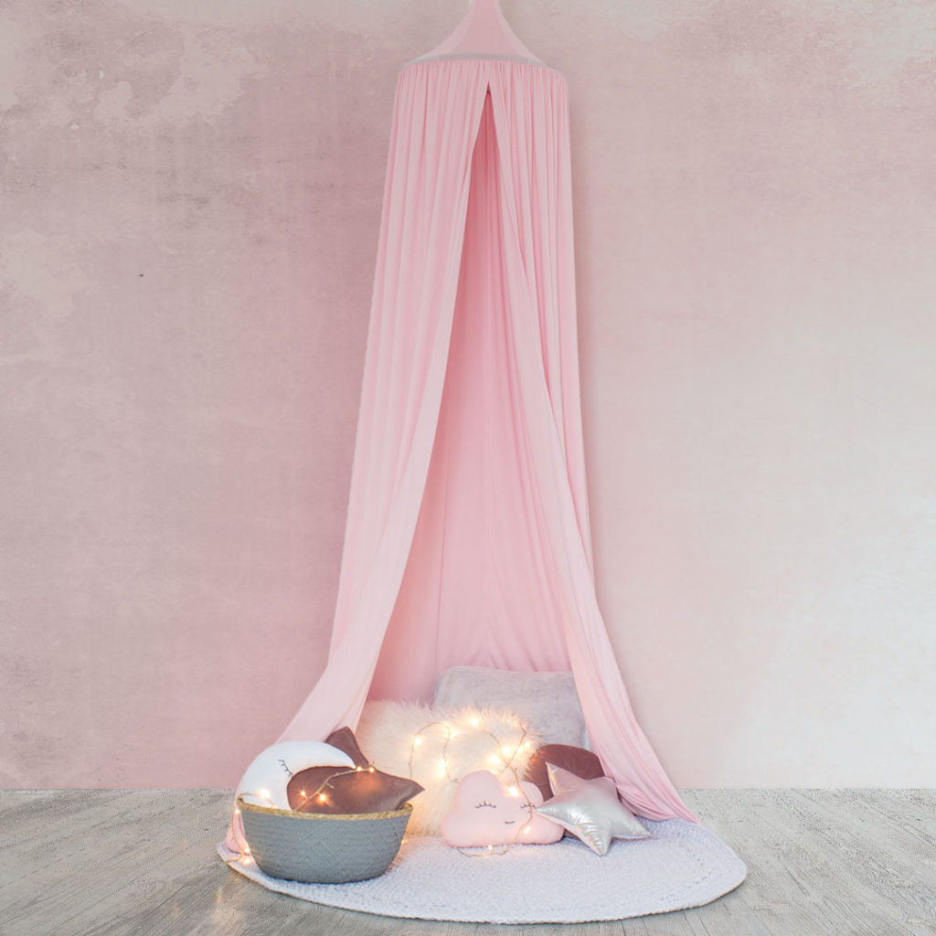 A pastel pink hanging tent canopy set up over a small table with a book and a decorative starfish, with dimly lit candles adding a warm glow.