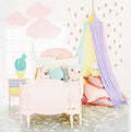 A pink-themed room with a white canopy featuring a unicorn design, hung over a bed with a purple blanket and pillows. The room also includes a yellow chair and a green plant.