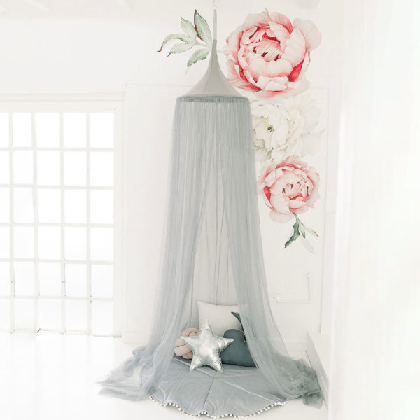 A grey hanging tent canopy with floral netting patterns set up in a room with two large pink artificial roses and a small cushion underneath.