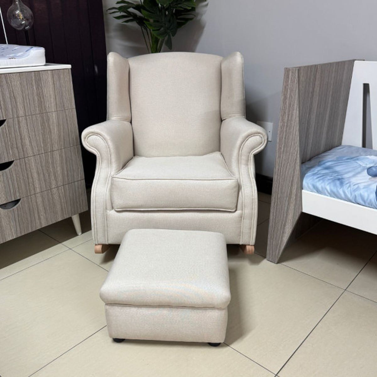 Beige armchair and ottoman in a room with a bed and dresser.