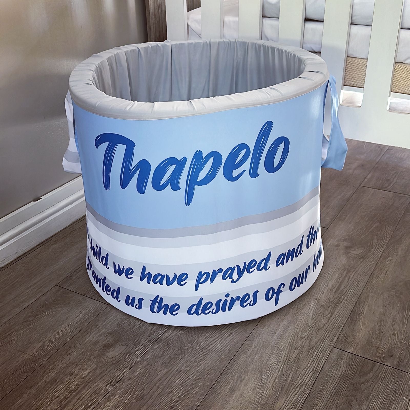 Round baby laundry barrel with 'Thapelo' branding on a wooden floor.