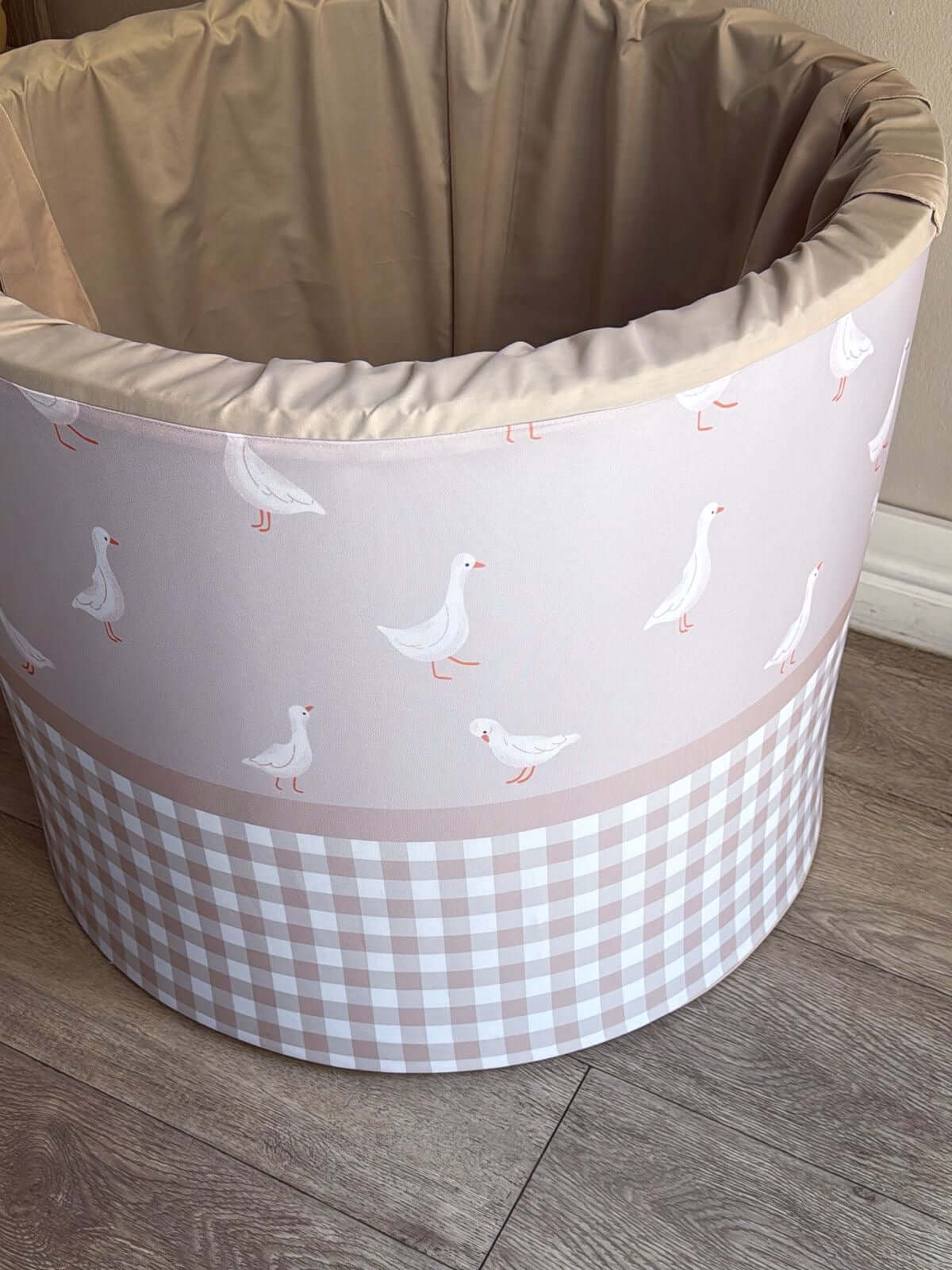Round fabric laundry barrel with goose pattern on a wooden floor