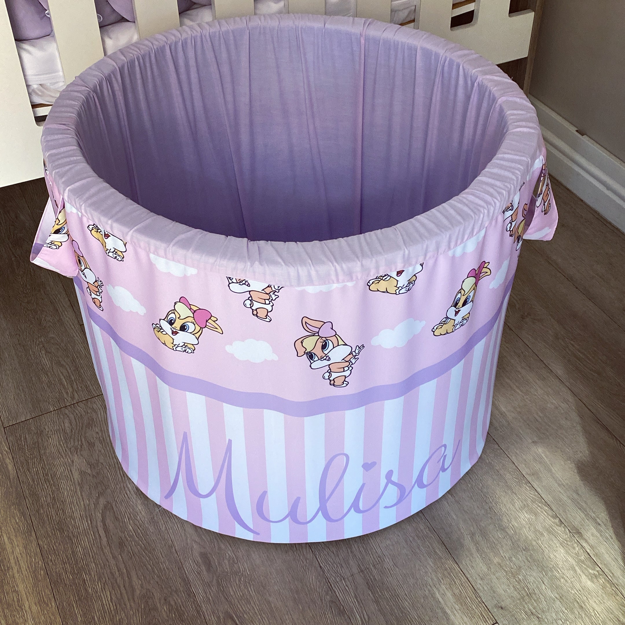 A large, round laundry basket with a purple base and a bunny-themed design, featuring cartoon images of bunnies and the name 'Mulisa' printed on the side.