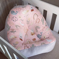 A pink boho-style baby lounger with a pattern of animals and plants, placed in a wooden crib.