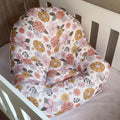 A floral-patterned lounger for babies, with a mix of pink and orange flowers on a white background, placed in a white crib.
