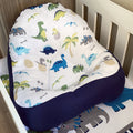 A dinosaur-themed baby lounger with a predominantly white fabric featuring colorful dinosaur prints and a solid blue cushion base.