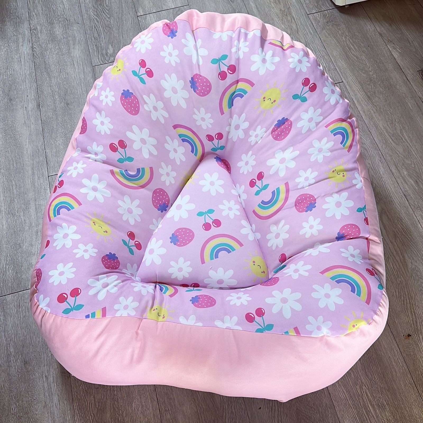 Pink baby seat with floral and rainbow patterns on a wooden floor
