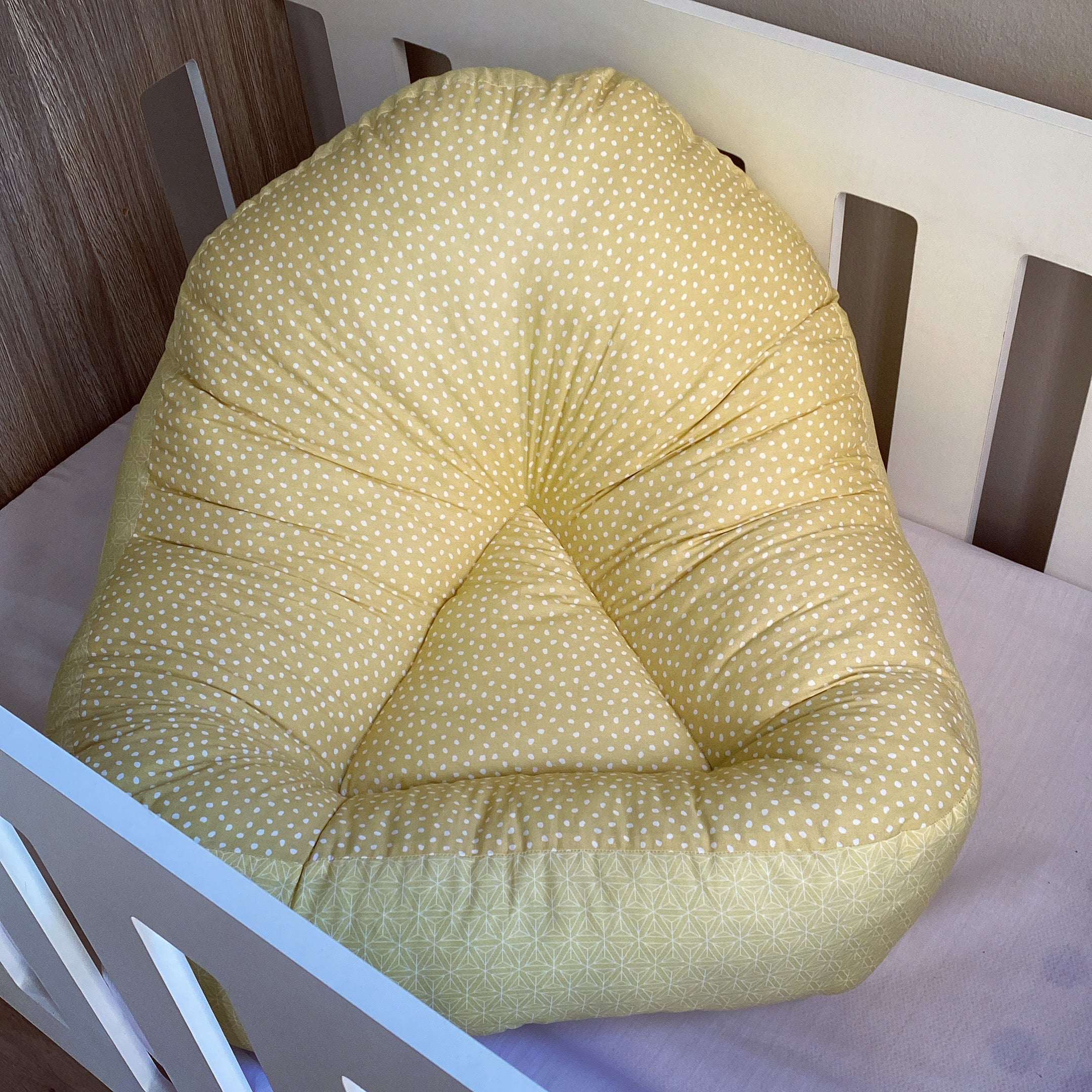 A yellow lounger with mustard dots pattern placed in a white crib.