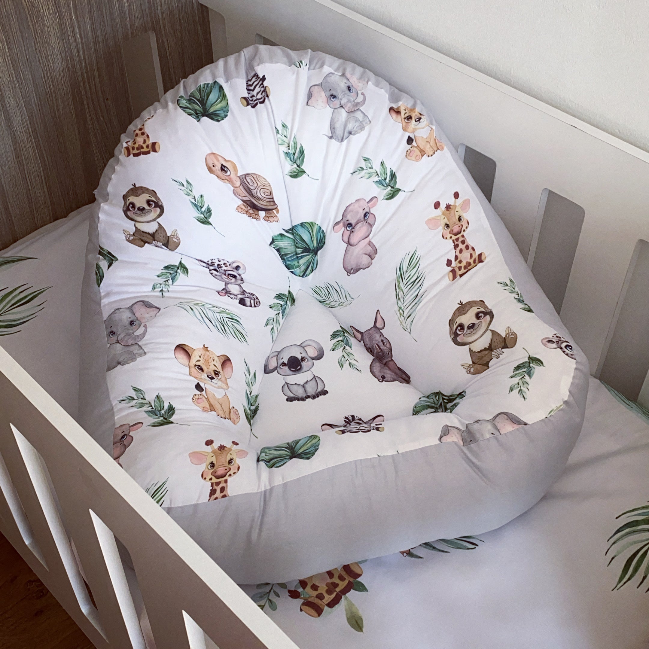 A safari-themed baby lounger with a white fabric featuring colorful animal illustrations, placed in a white crib.