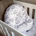 A white fabric lounger with a sheep pattern, positioned in a wooden crib.