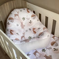 A white fabric lounger with a woodland animal print, positioned in a wooden crib.