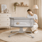 Woman interacting with a baby in a grey dream starlight bassinet in a nursery setting.