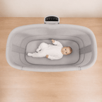 Baby in a gray bassinet on a wooden floor
