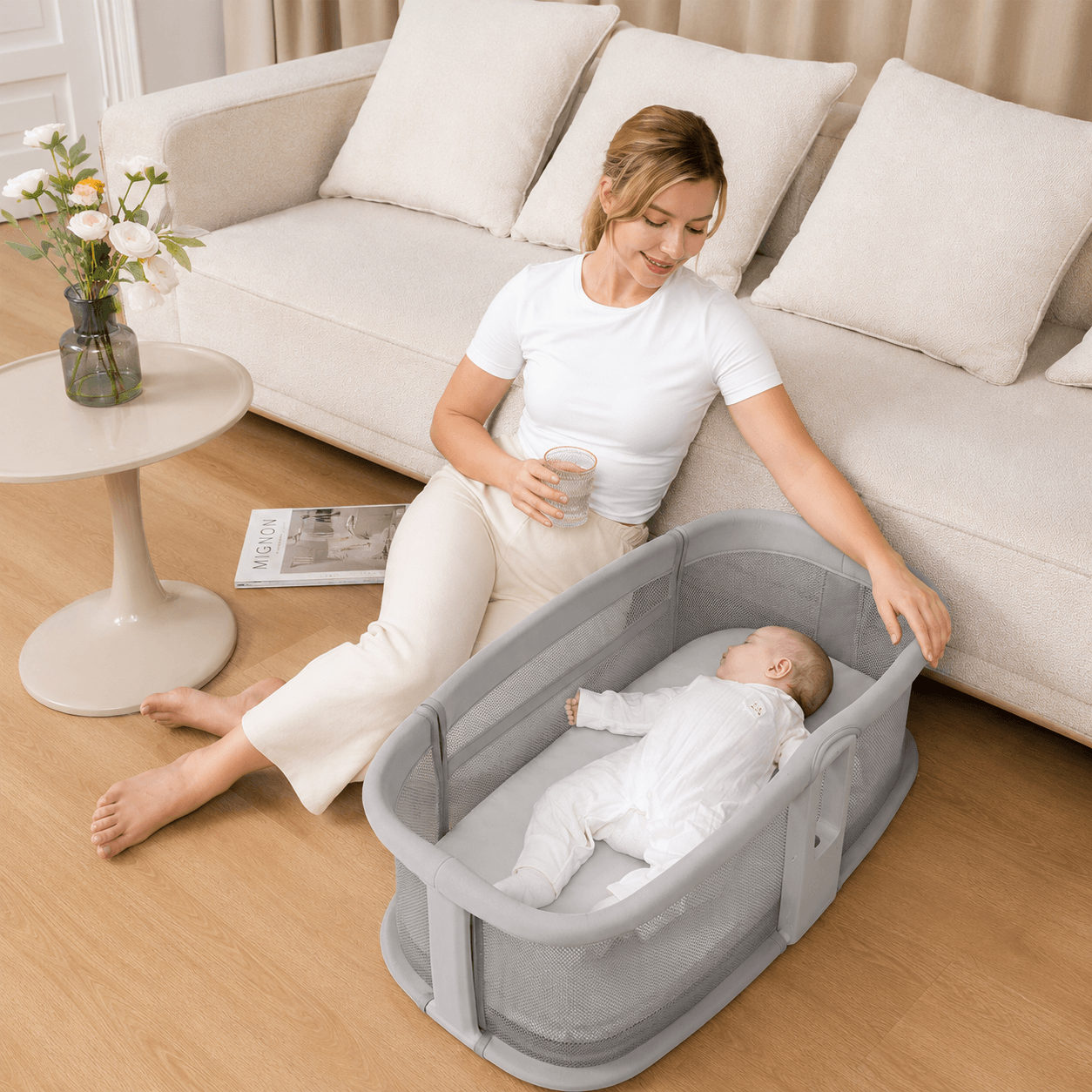 Woman sitting on the floor with a baby in a portable dream starlight bassinet in a living room.