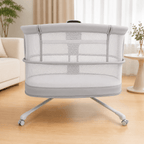 Portable dream starlight crib with mesh sides on a wooden floor in a room with a couch and plants.