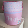 A pink laundry basket with a pattern of rainbows, clouds, and an elephant, and the word 'THINGO' printed on it.