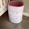 A pink laundry barrel with a rainbow and unicorn pattern, placed in a room corner with a wooden floor and a pink wall.