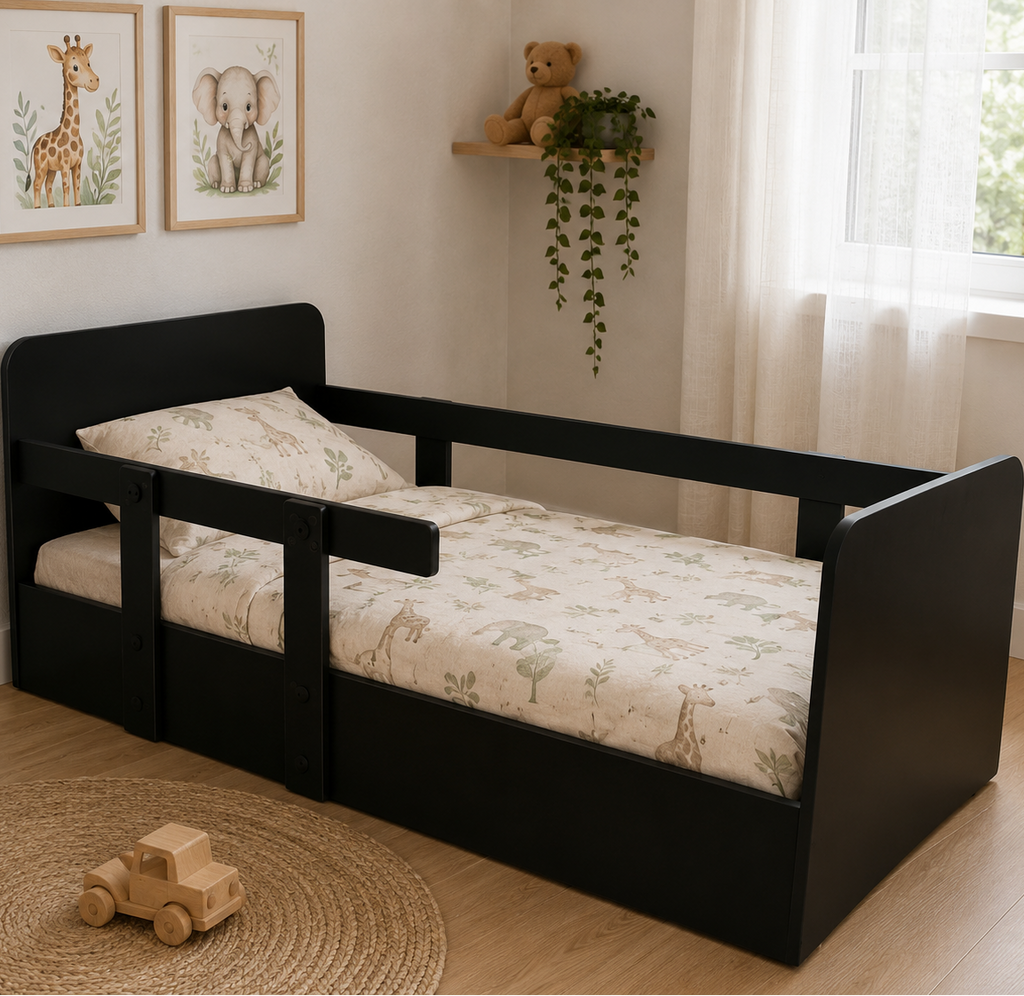 A toddler bed with a black wooden frame and safety rails, dressed in a light beige forest-patterned sheet and pillow, set in a bright children's bedroom.