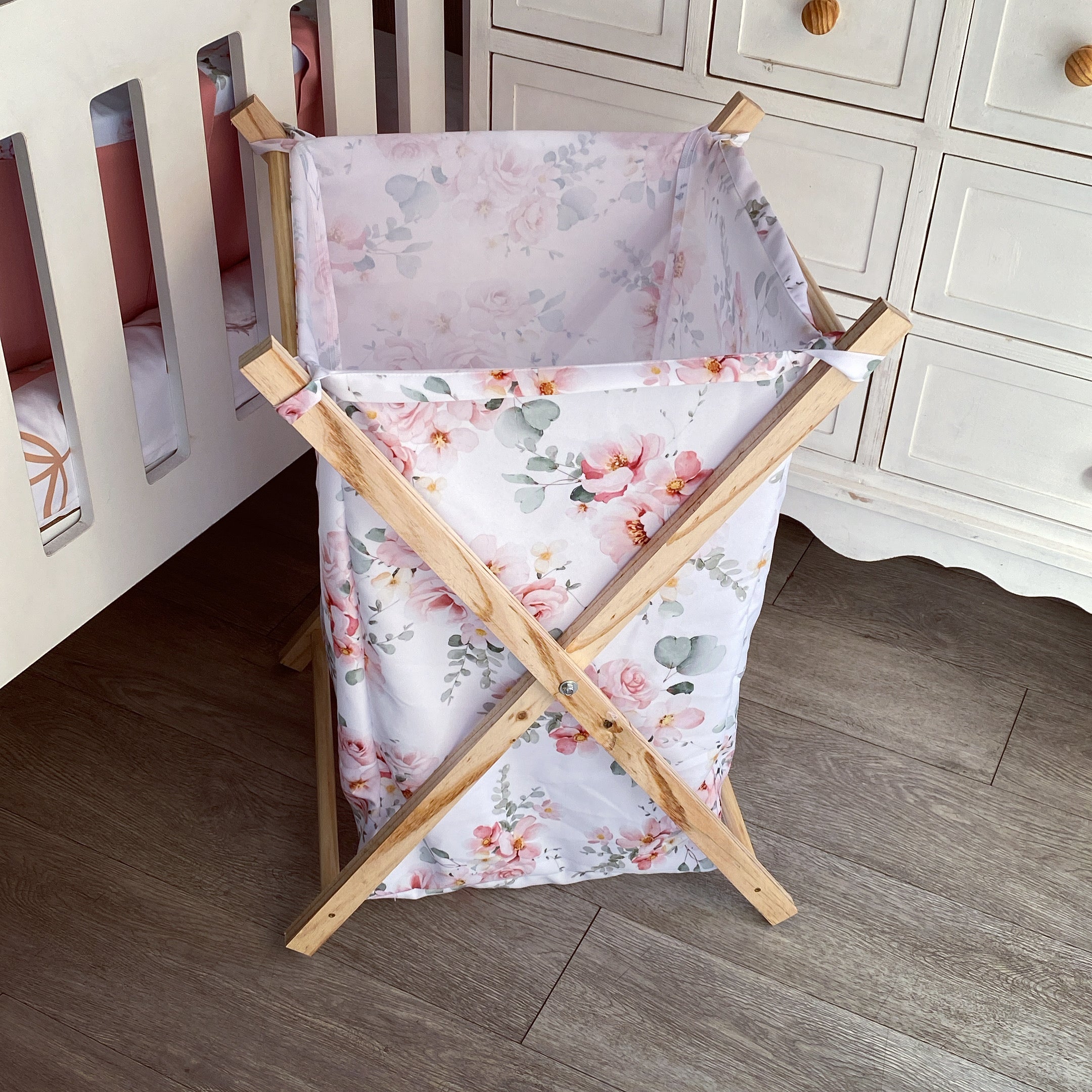 A wooden laundry basket with a pink floral pattern, featuring side handles and a five-point star base.