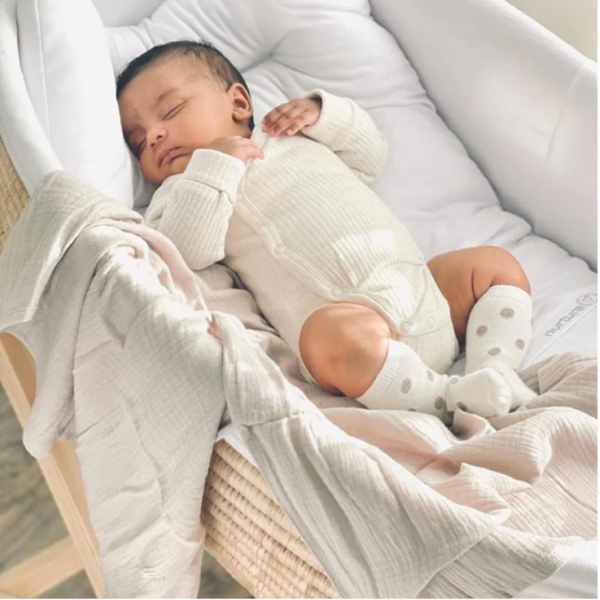 Newborn baby sleeping in a crib with white bedding and light clothing.