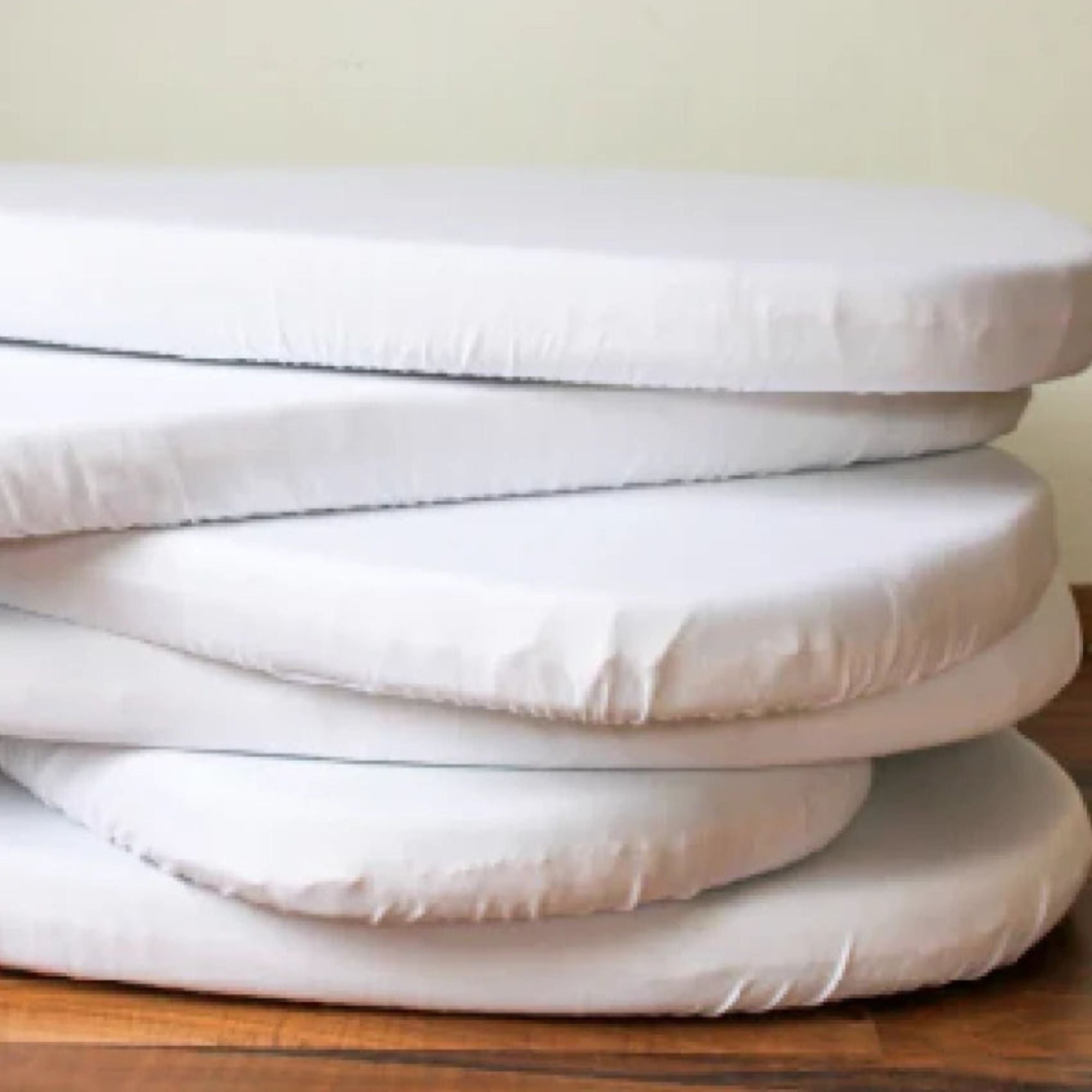 Stack of white mattress toppers on a wooden surface with a neutral background