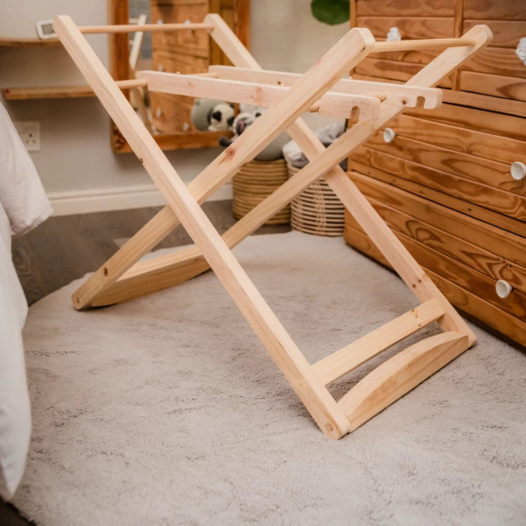 Wooden folding laundry rack on a carpeted floor with wooden furniture in the background.