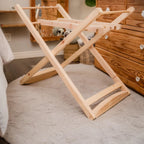 Wooden folding laundry rack on a carpeted floor with wooden furniture in the background.