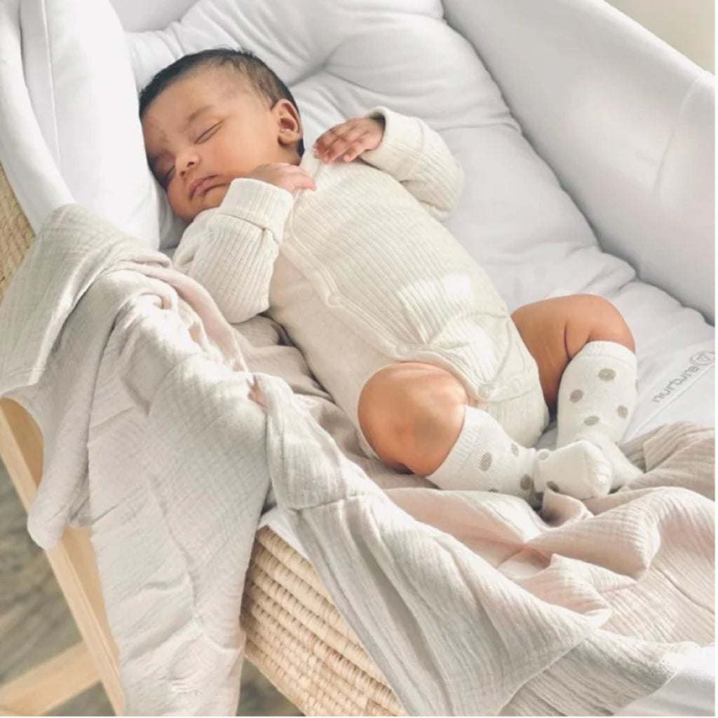 Newborn baby sleeping in a crib with white bedding and light clothing.